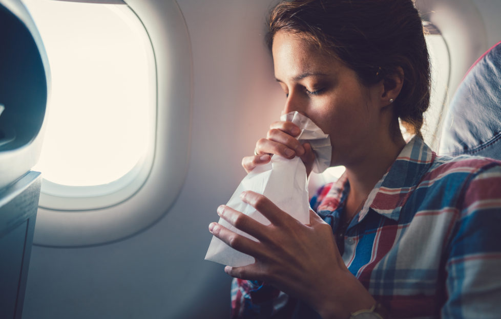 Young woman feeling bad during a flight and breathing in vomit bag