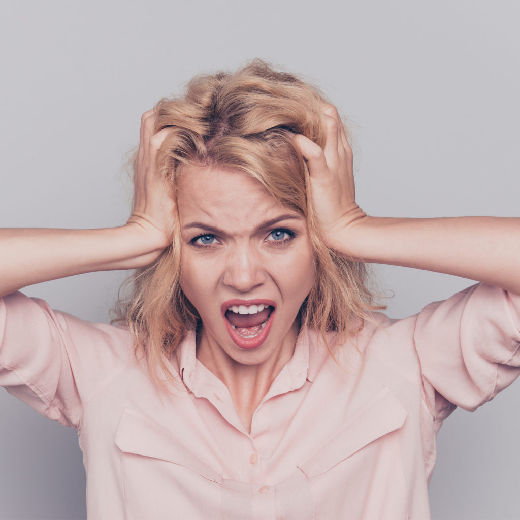 Blonde woman shouting in anger and frustration, hands to her head