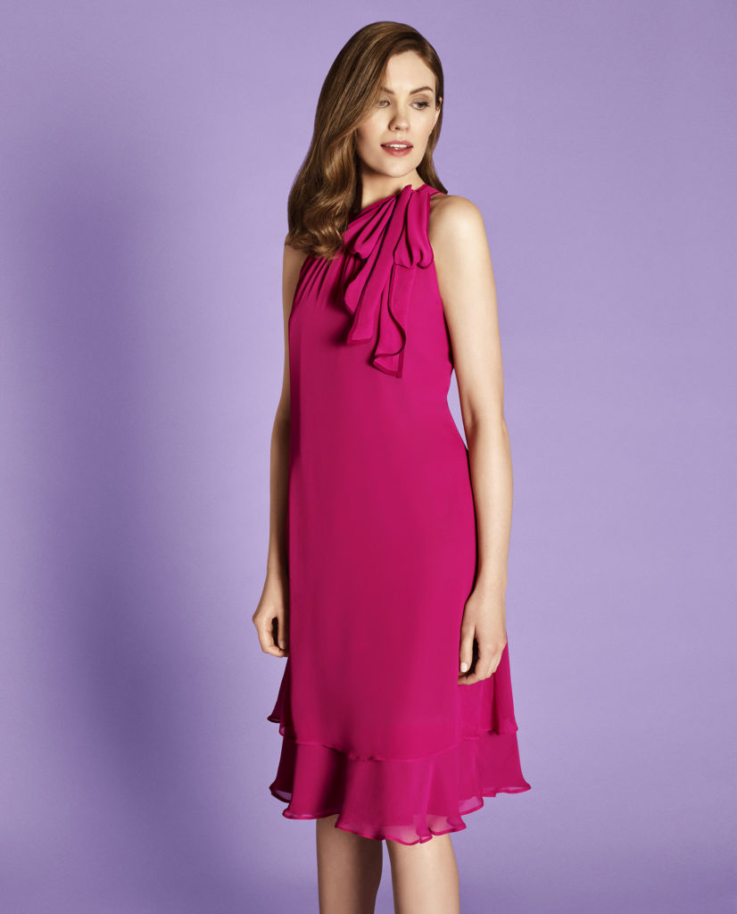 Woman in sleeveless cerise dress, two layered hem just below knee, soft pleated ruffle hanging from left shoulder