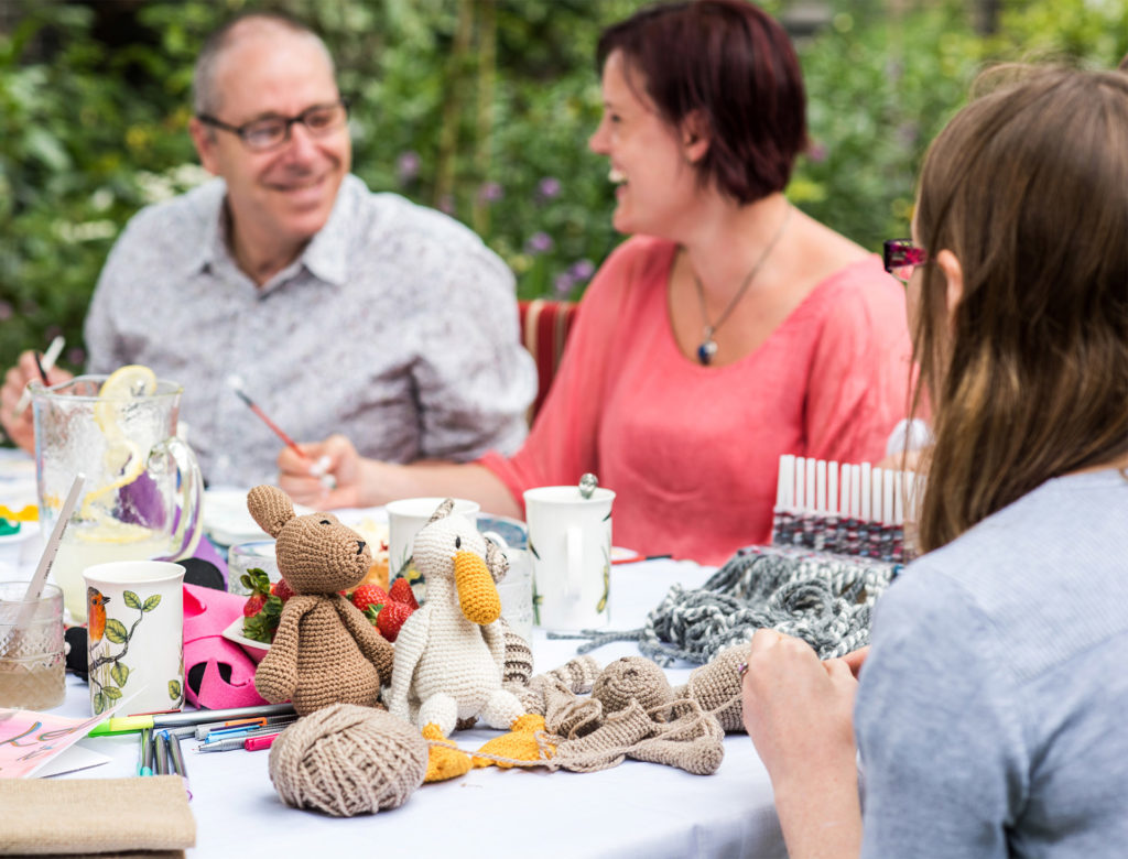 Girl assembling crocheted pieces into a small dog while others chat at a Crafternoon event