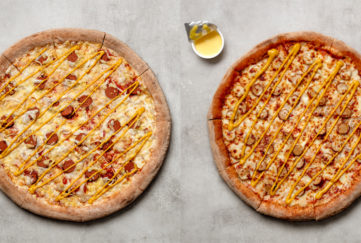 Two hotdog pizzas. The vegan version has pale cheese and reddish hotdog pieces and the regular version has darker toasted cheese and pale pink hotdog pieces