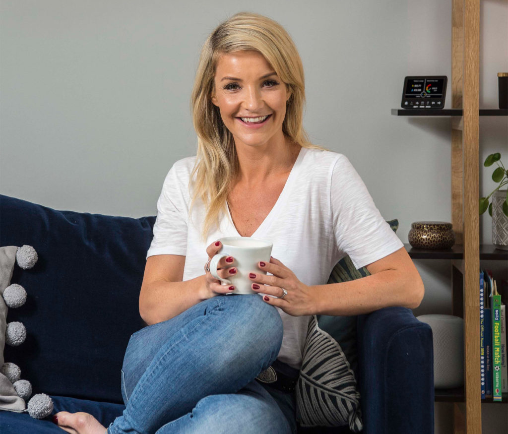 Countryfile presenter Helen Skelton sitting on a black leather sofa with a mug of tea. One of her energy saving tips is not to fill the kettle with more water than you need.