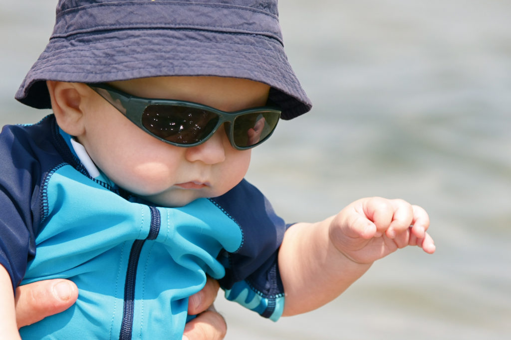 "A baby boy, wearing sunglasses and a sun hat, enjoys a day at the beach. 