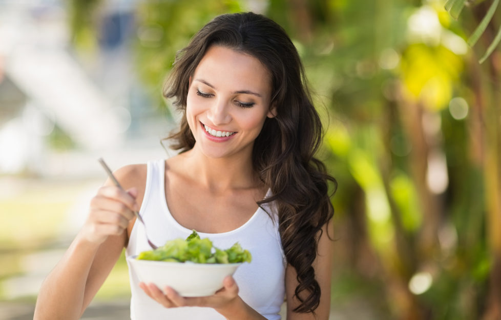 Pretty brunette eating bowl of salad on a sunny day