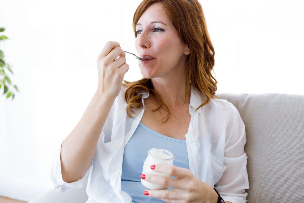 Portrait of beautiful young woman eating yogurt at home.