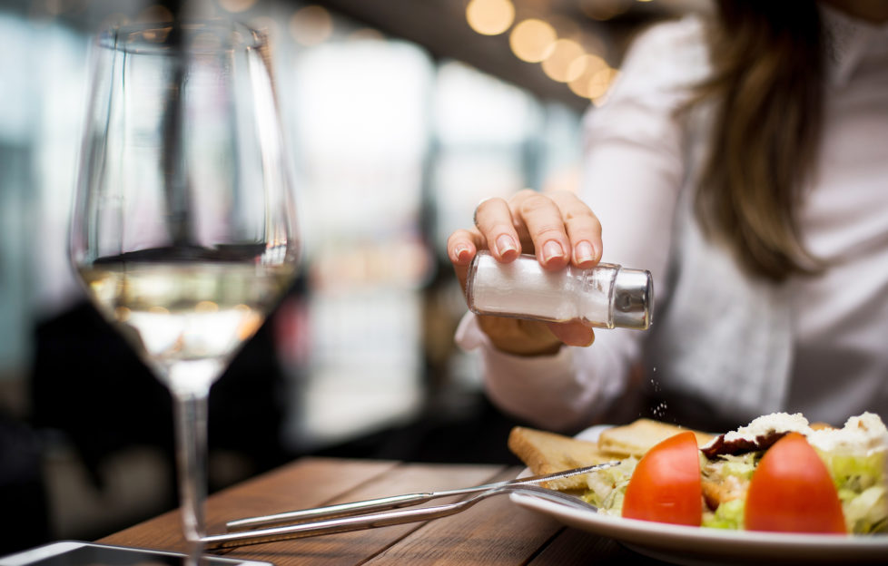 Woman adding salt to food in restaurant.