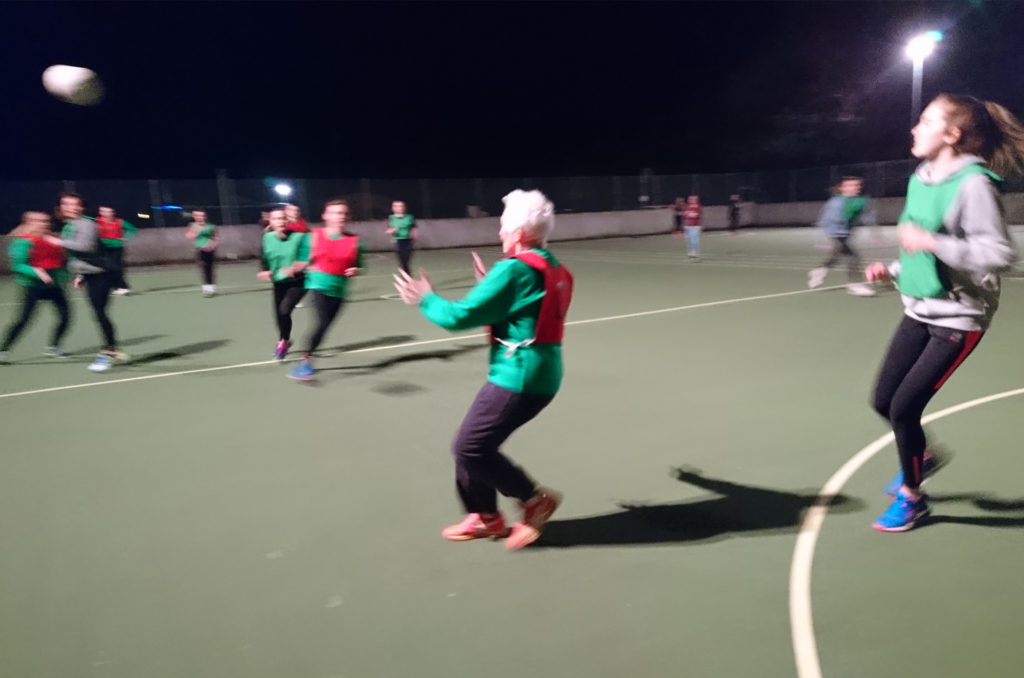 Elderly lady playing netball, about to catch the ball, other players in background