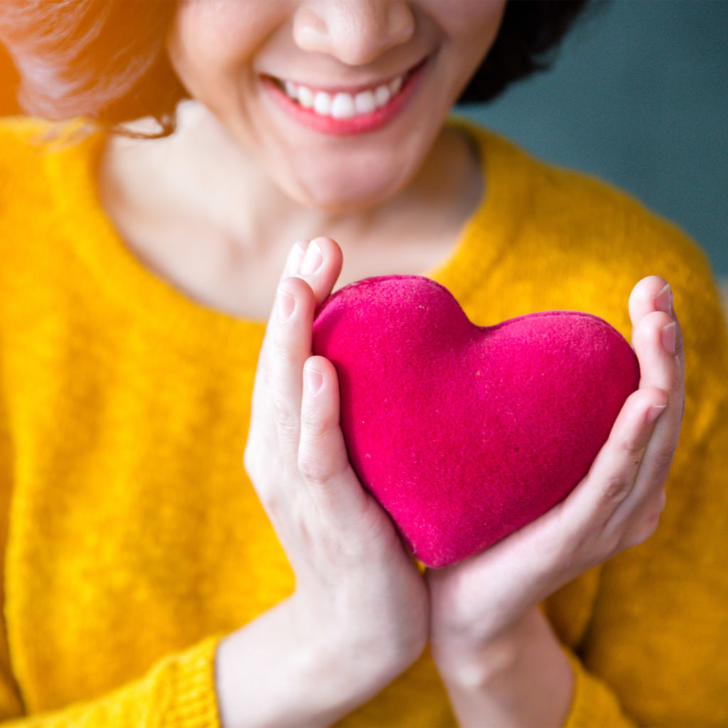 close up of woman in yellow sweater holding small red heart cushion
