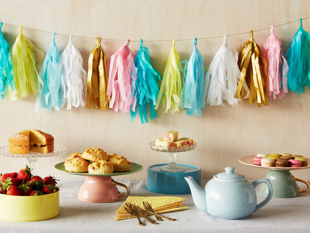 Table with teapot, cups and plates of cakes, string of handmade streamer decorations on wall behind, all ready for a Crafternoon event