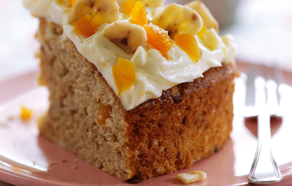 Slice of banana cake decorated with cream icing, banana chips and pieces of apricot