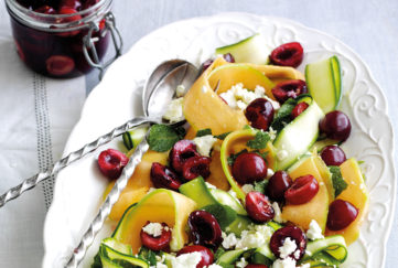 Serving bowl of cherry salad with ribbons of orange melon and courgette and crumbled feta cheese