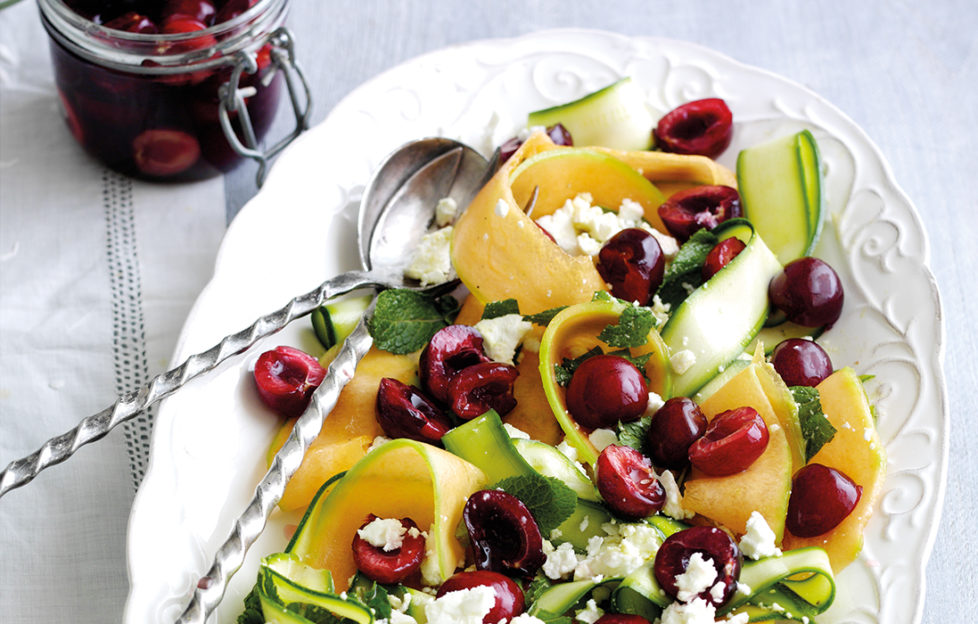 Serving bowl of cherry salad with ribbons of orange melon and courgette and crumbled feta cheese
