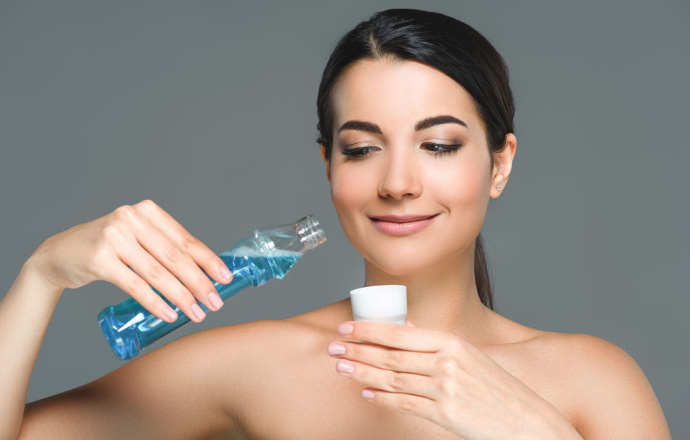 portrait of smiling woman with bare shoulders holding mouthwash isolated on grey