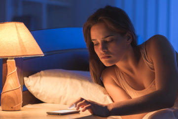 Woman in bed in night checking phone at bedside