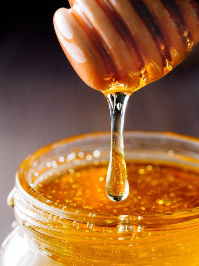 Honey dripping from honey-dipper in glass jar. 