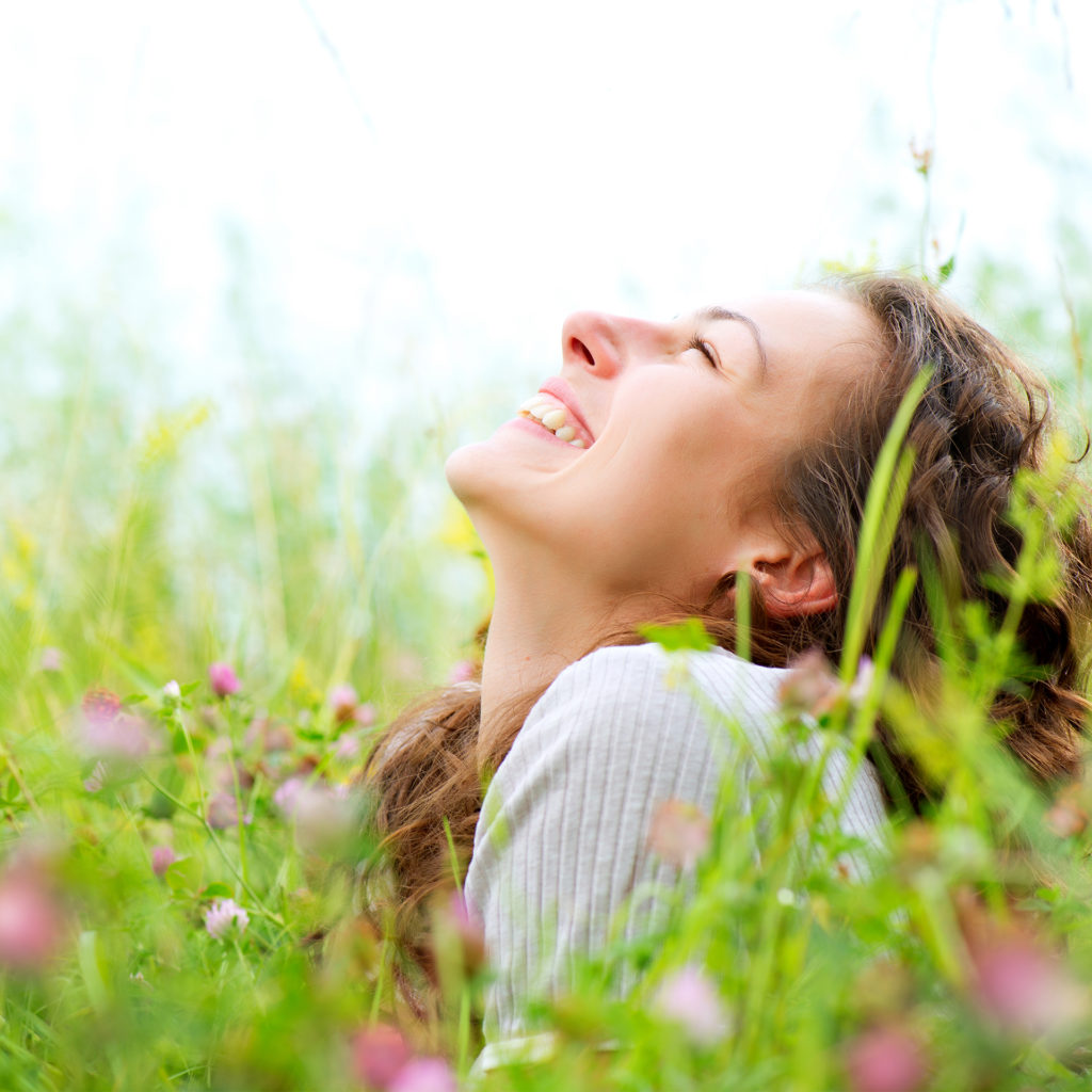Happy woman sitting in a wildflower meadow looking up at the sky
