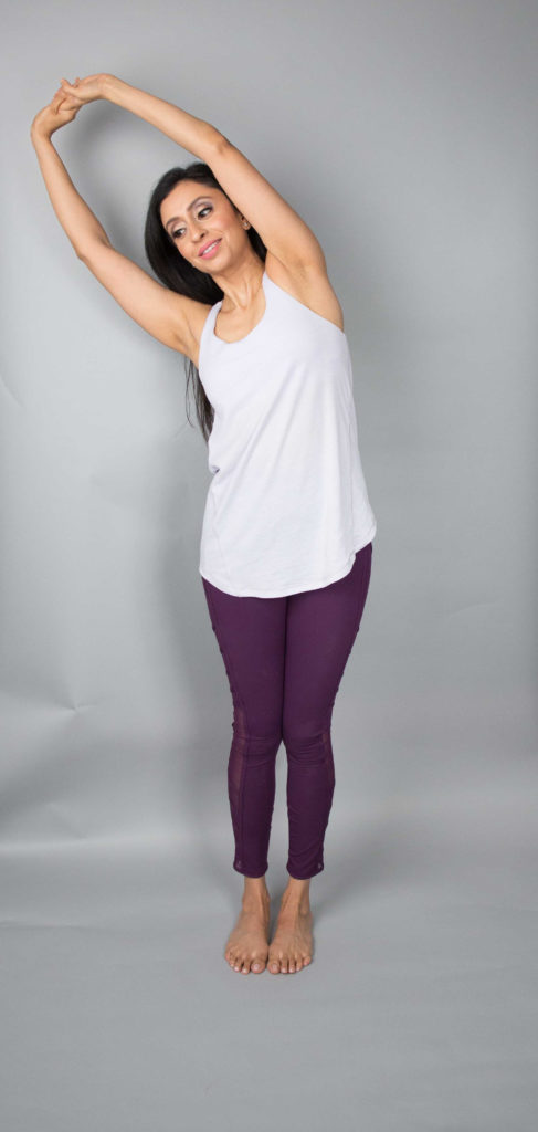 Woman doing side stretch with arms about head and standing