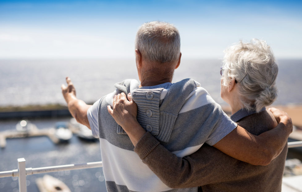 Senior man pointing at beach while embracing his wife by seaside