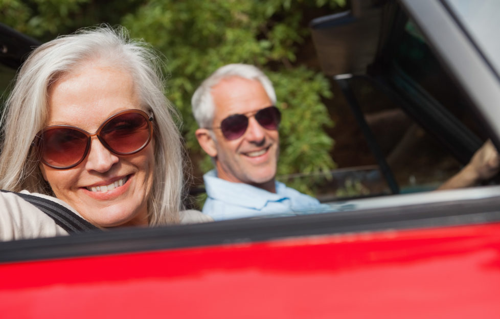 Side view of cheerful mature couple driving red cabriolet on sunny day