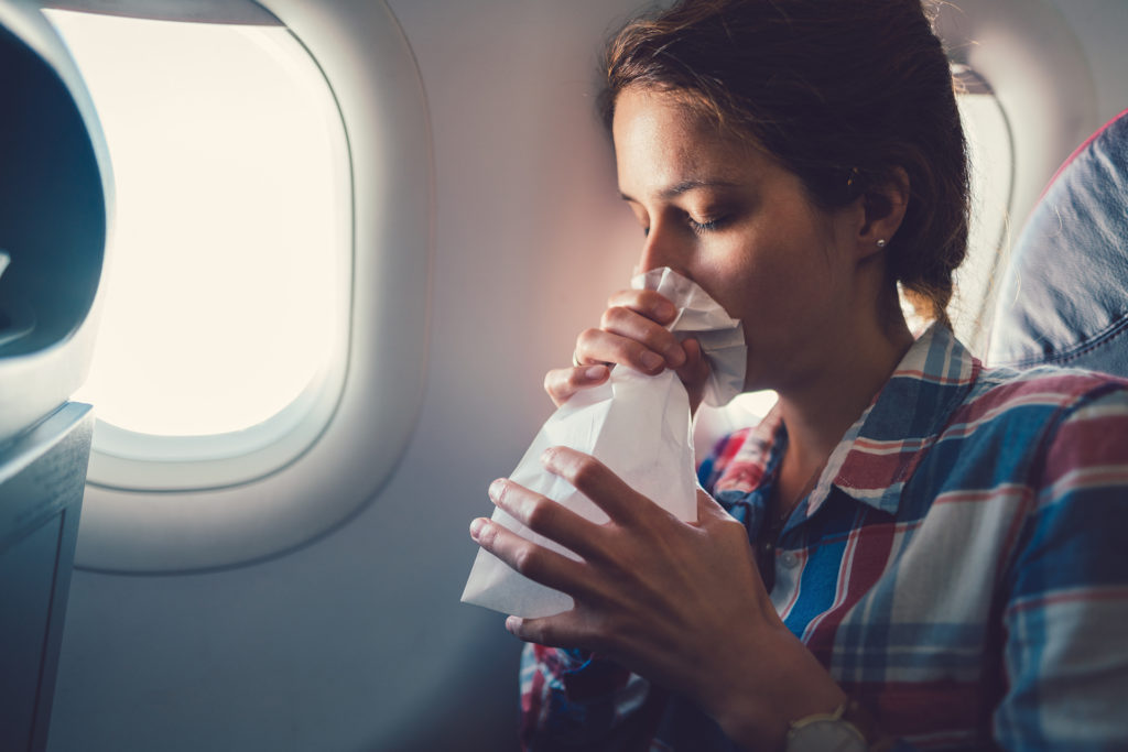 Young woman feeling bad during a flight and breathing in vomit bag