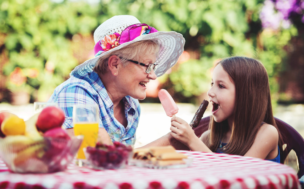 Happy little girl and her grandmother eating ice cream, having fun together in the garden. 