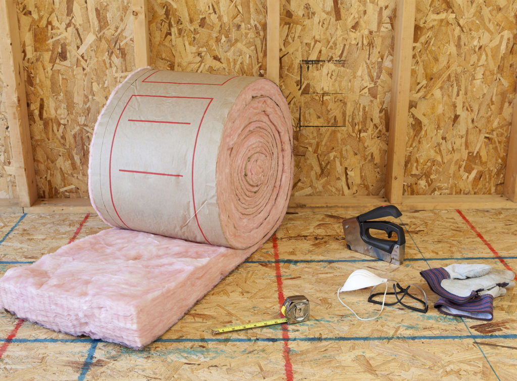 roll of insulation material on a chipboard floor, tools, gloves and mask nearby