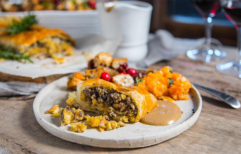 Slice of lentil and mushroom wellington wrapped in golden pastry, on a plate with sweet potato mash and salad