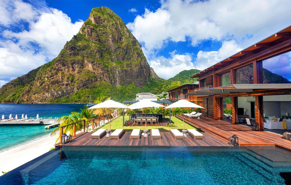 Sugar Beach, A Viceroy resort - steep, wooded mountain behind, holiday home with decking over turquoise water in foreground