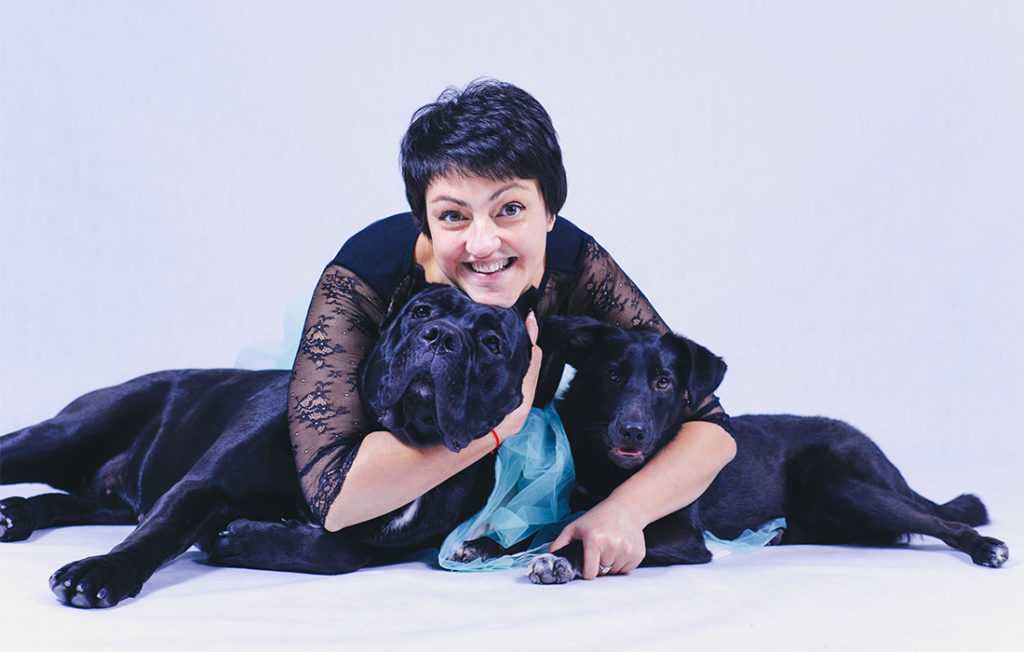 Pets make life happier. Happy mature woman lying on floor hugging two happy black dogs