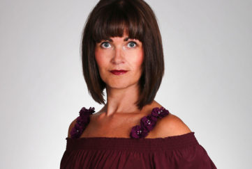 Head and shoulders of model in burgundy blouse, flower trimmed cami straps showing