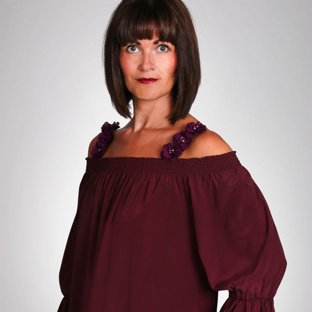 Model in burgundy blouse, wide elasticated neck pulled down over shoulders,burgundy flower-trimmed straps of camisole visible