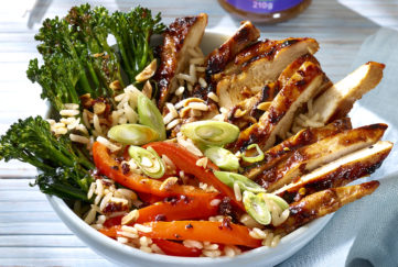 Sliced chicken with dark glaze, broccoli, red peppers, rice and spring onions arranged in groups in a bowl