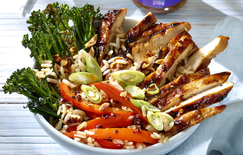 Sliced chicken with dark glaze, broccoli, red peppers, rice and spring onions arranged in groups in a bowl