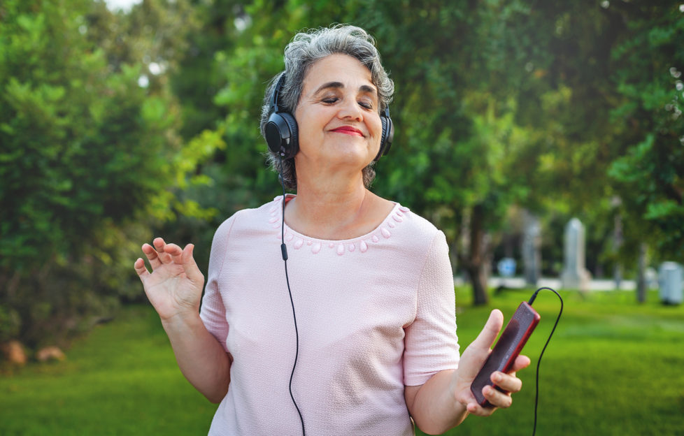 Senior woman listening music with headphones in the park