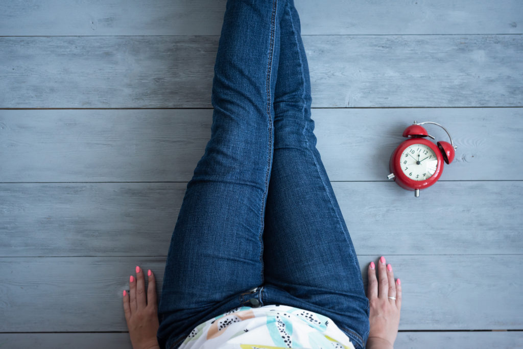 Tired woman and red alarm clock on a wooden floor background.