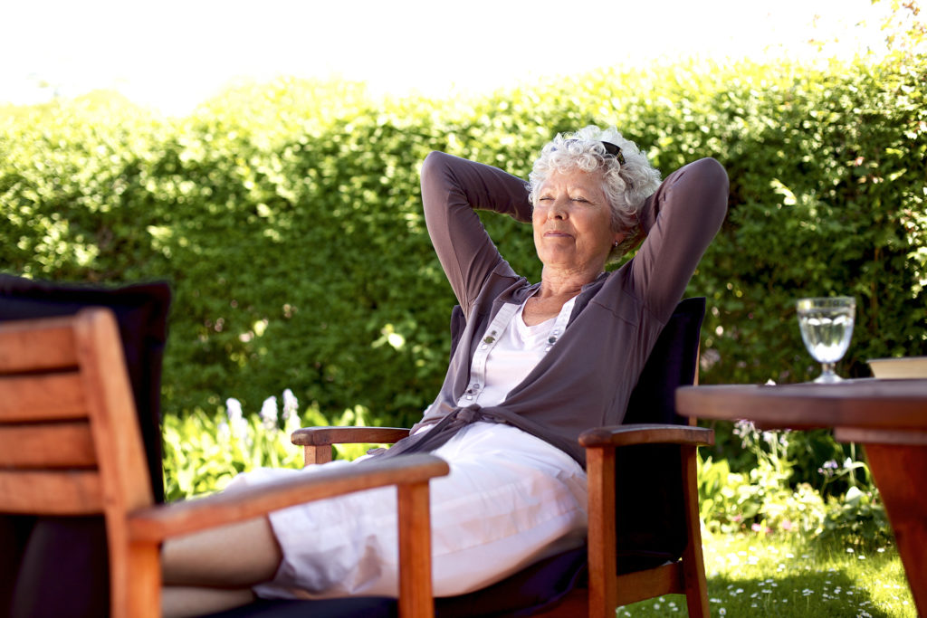 Senior woman sitting on a chair and taking a nap in backyard. Elder woman sleeping in backyard garden