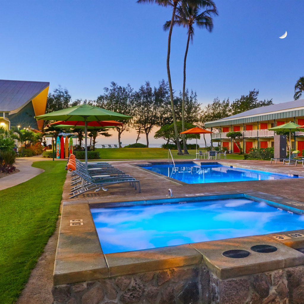 Two square swimming pools at dusk in beachside hotel with palm trees