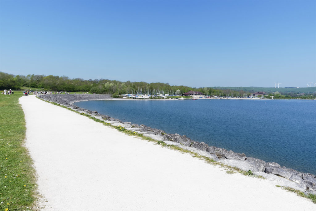 White gravel path beside blue water, boat yards in distance