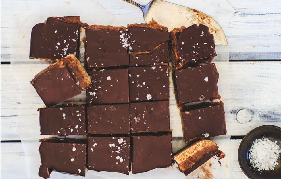 Millionaire's shortbread on baking paper, cut into 16 squares, one turned sideways to show biscuit, caramel and chocolate layers