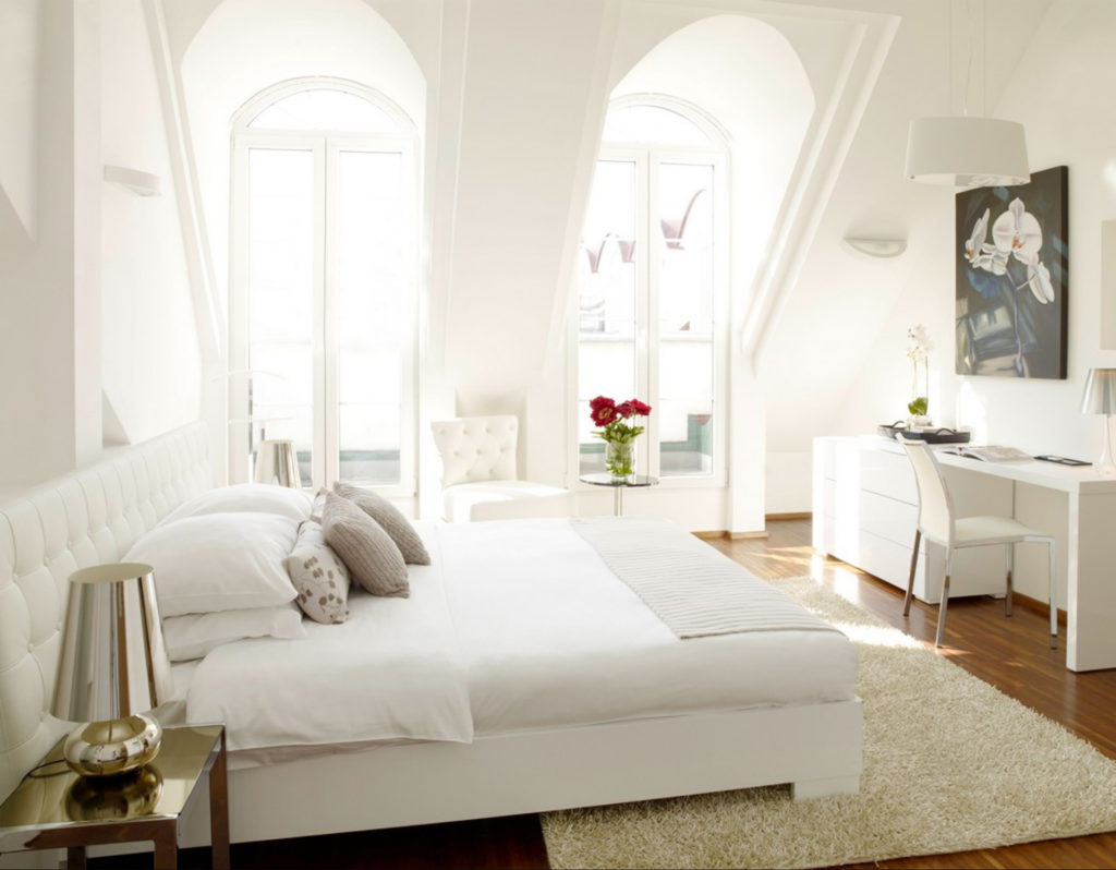 Completely white room with double bed and desk,light pouring through two high arched windows