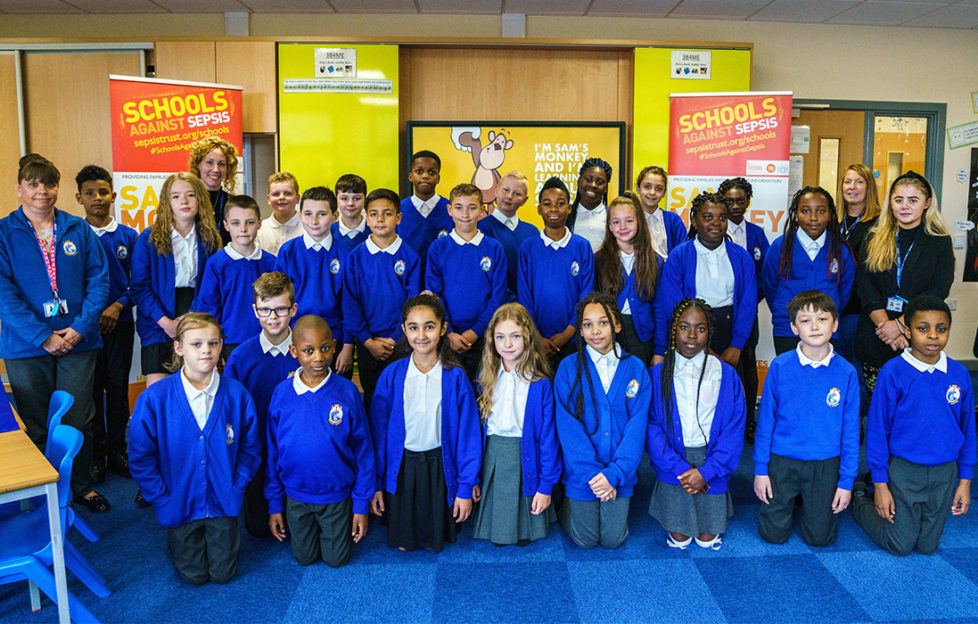 Class of pupils pose in front of sepsis awareness display