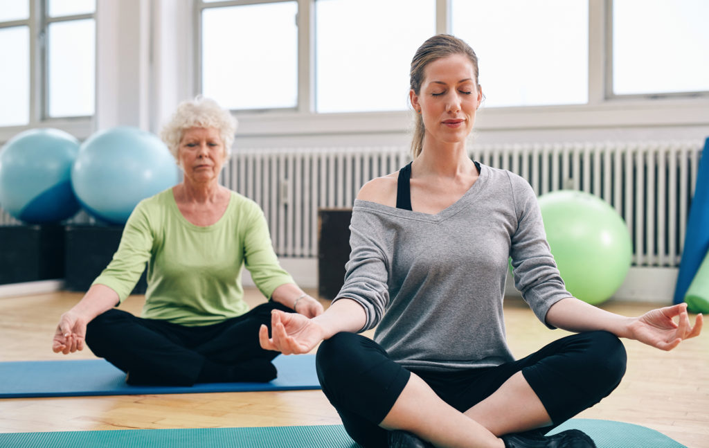 Two women practicing yoga in class. Female trainer and senior woman sitting in lotus position meditating.