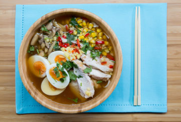 Bowl of chicken ramen noodles with halved boiled egg, sweetcorn and fresh coriander garnish