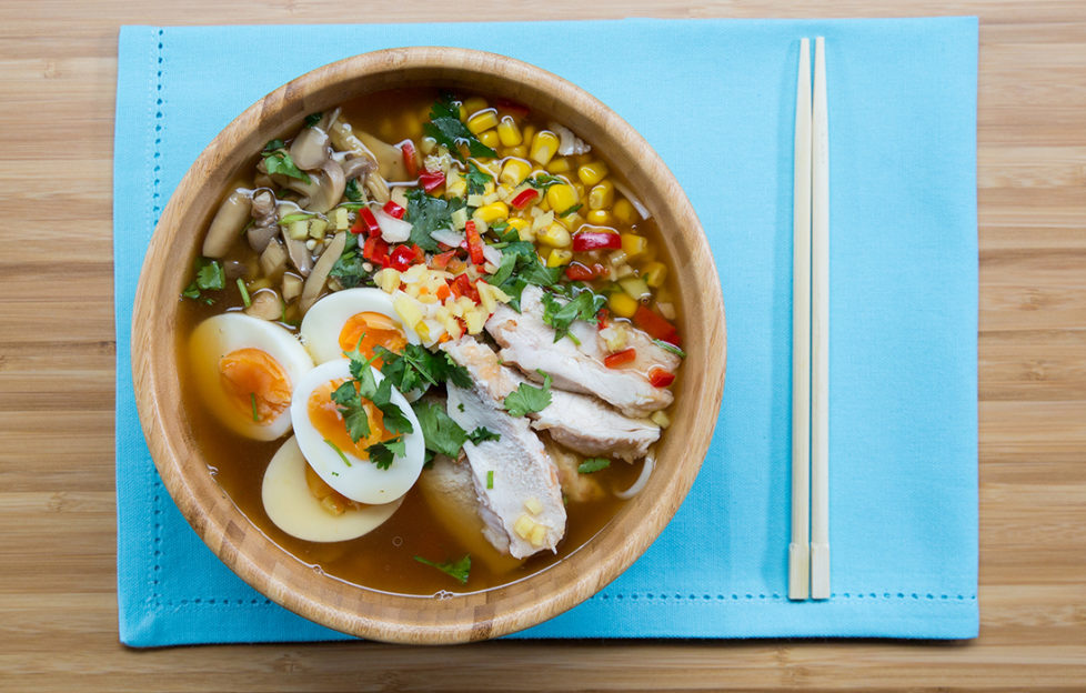 Bowl of chicken ramen noodles with halved boiled egg, sweetcorn and fresh coriander garnish
