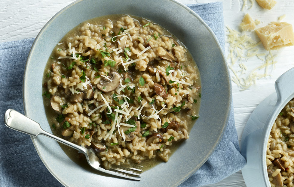 Bowl of rich brown mushroom risotto garnished with grated cheese and chopped parsley