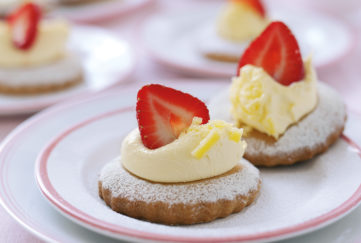 Small plate with two round shortcake biscuits, each decorated with whipped cream and half a strawberry