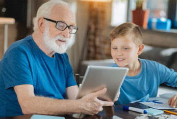 grandfather with white beard and glasses shows grandson something on electronic tablet