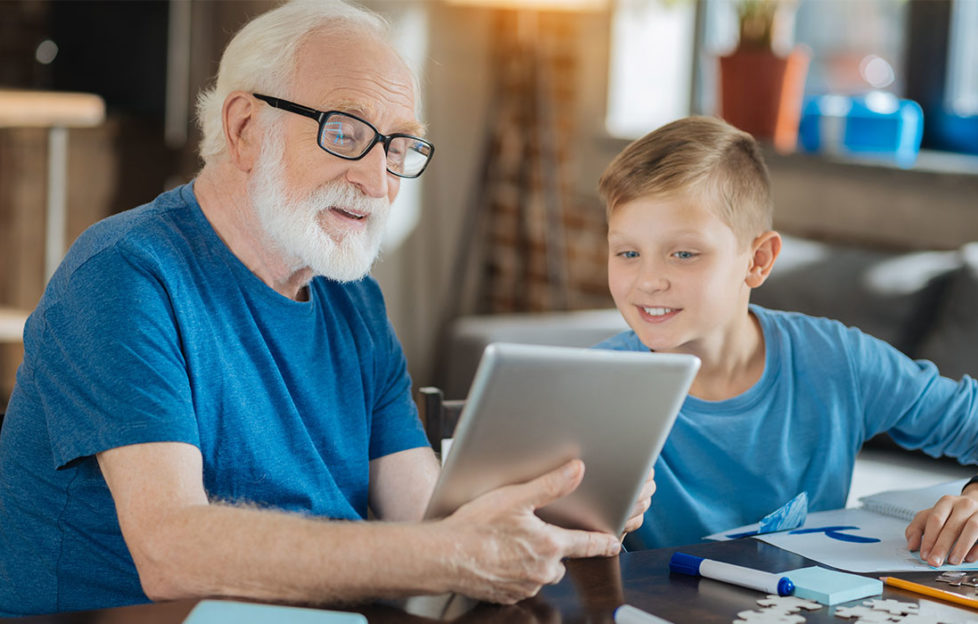 grandfather with white beard and glasses shows grandson something on electronic tablet