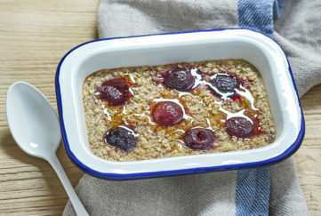 Rectangular enamel dish containing oats studded with cherries and drizzled with maple syrup