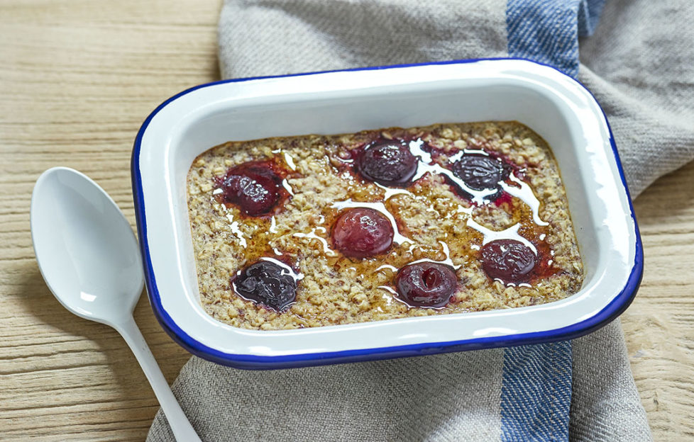 Rectangular enamel dish containing oats studded with cherries and drizzled with maple syrup